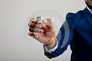 Mid section of businessman holding bulb screw base against grey background