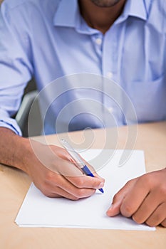 Mid section of businessman writing document at desk