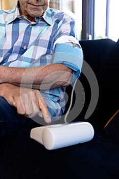 Mid section of caucasian senior man checking his blood pressure sitting on the couch at home