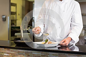 Mid section of a chef garnishing food in kitchen