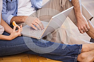 Mid section of couple sitting on floor using laptop