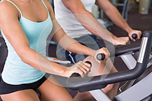 Mid section of couple working on exercise bikes at gym