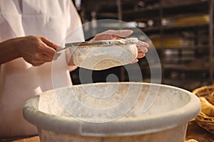 Mid-section of female baker sifting flour through a sieve