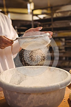 Mid-section of female baker sifting flour through a sieve