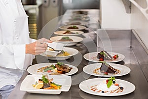 Mid section of a female chef garnishing food in kitchen