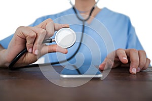 Mid-section of female doctor examining mobile phone with a stethoscope