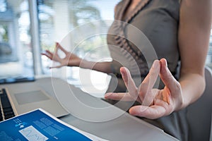 Mid section of female executive performing yoga at desk
