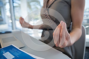 Mid section of female executive performing yoga at desk