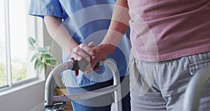 Mid section of female health worker assisting senior woman to walk with walking frame at home