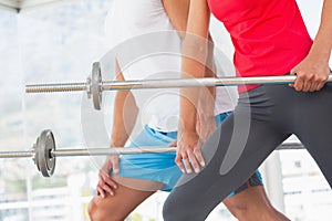 Mid section of fit young couple holding barbells