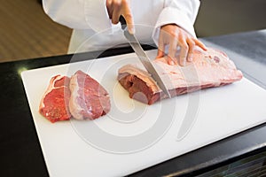 Mid section of hands cutting meat in kitchen