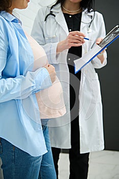 Mid-section image. Unrecognizable female doctor explaining ultrasound scan results to pregnant woman in obstetric clinic