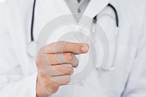 Mid section of a male doctor holding acupuncture needles