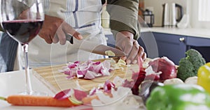 Mid section of man wearing apron chopping vegetables in the kitchen at home