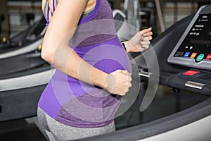 Mid section of pregnant woman running on treadmill