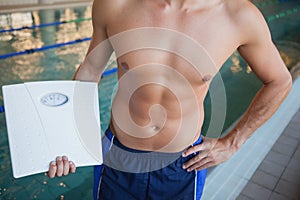 Mid section of a shirtless fit swimmer with weighing scales by pool