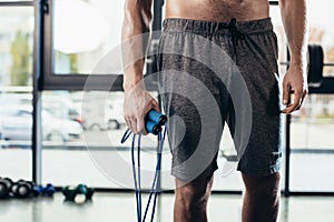 mid section of shirtless sportsman holding jumping rope