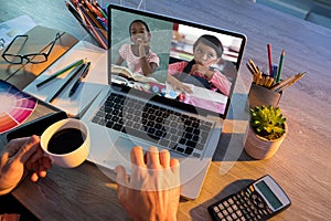 Mid section of teacher having a video conference with two female students on laptop at school