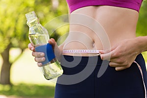 Mid section of a toned woman measuring waist in park