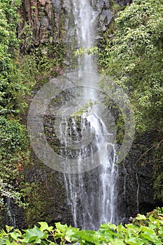 The mid-section of Wailua Falls cascading down a rocky, volcanic cliffside in a rainforest in Hana, Maui, Hawaii