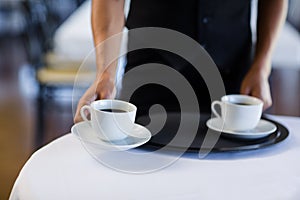 Mid section of waitress serving cup of coffee