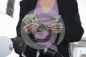 Mid Section Of A Woman Refueling Her Car While Counting Money