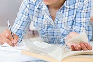 Mid section of young female student doing assignments while lying on the floor photo