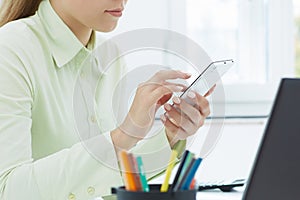 Mid section of the young woman holding smartphone. Stylish modern office workplace on a background.