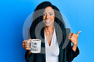 Middle age african american woman drinking from i am the boss coffee cup pointing thumb up to the side smiling happy with open