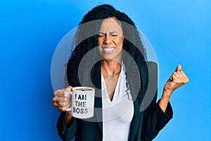 Middle age african american woman drinking from i am the boss coffee cup screaming proud, celebrating victory and success very