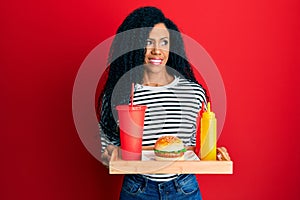 Middle age african american woman eating a tasty classic burger smiling looking to the side and staring away thinking