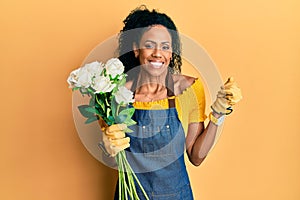 Middle age african american woman holding bouquet of white roses flowers screaming proud, celebrating victory and success very