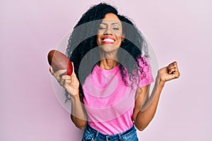 Middle age african american woman holding mango screaming proud, celebrating victory and success very excited with raised arm