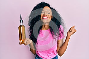 Middle age african american woman holding olive oil can screaming proud, celebrating victory and success very excited with raised