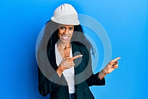 Middle age african american woman wearing architect hardhat smiling and looking at the camera pointing with two hands and fingers