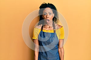 Middle age african american woman wearing professional apron afraid and shocked with surprise and amazed expression, fear and