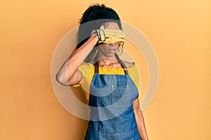 Middle age african american woman wearing professional apron covering eyes with hand, looking serious and sad