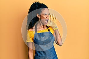 Middle age african american woman wearing professional apron shouting and screaming loud to side with hand on mouth