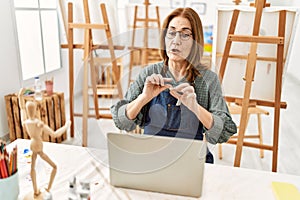 Middle age artist woman smiling happy having video call using laptop at art studio