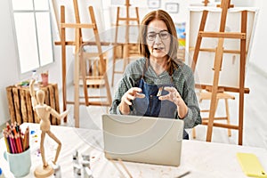 Middle age artist woman smiling happy having video call using laptop at art studio