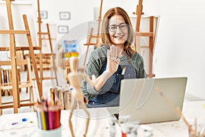 Middle age artist woman smiling happy having video call using laptop at art studio