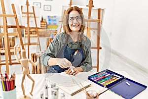 Middle age artist woman smiling happy painting sitting on the table at art studio