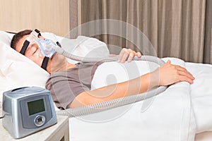 middle age asian man sleeping in bed wearing CPAP mask connecting to air hose and CPAP machine, device for people with sleep apnea