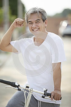 Middle age asian man toothy smiling face happiness emotion exercise by riding bicycle in home village street