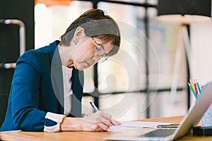 Middle age Asian woman working on paperwork in modern office, with laptop computer. Business owner or entrepreneur concept