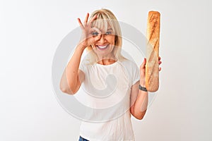 Middle age baker woman holding bread standing over isolated white background with happy face smiling doing ok sign with hand on