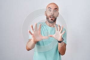 Middle age bald man standing over white background afraid and terrified with fear expression stop gesture with hands, shouting in