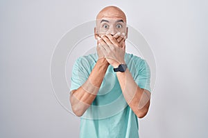 Middle age bald man standing over white background shocked covering mouth with hands for mistake