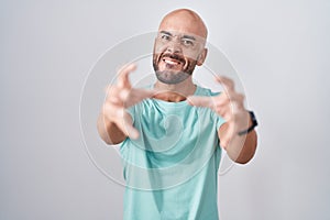 Middle age bald man standing over white background shouting frustrated with rage, hands trying to strangle, yelling mad