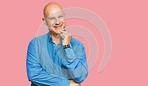 Middle age bald man wearing casual clothes looking confident at the camera smiling with crossed arms and hand raised on chin